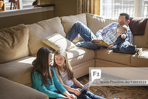 Father teaching son by sisters using tablet at home