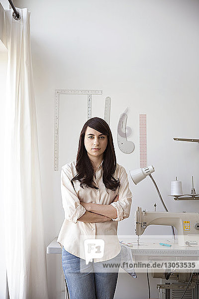 Porträt einer selbstbewussten Modedesignerin  die gegen eine Nähmaschine steht