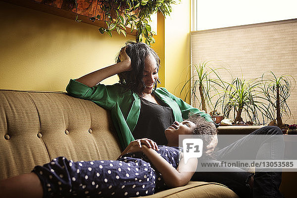 Mother looking at girl while relaxing on sofa at home