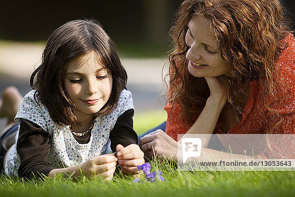 Mother and daughter talking while lying on grassy field