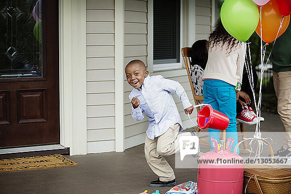Portrait of happy boy holding bucket running at porch