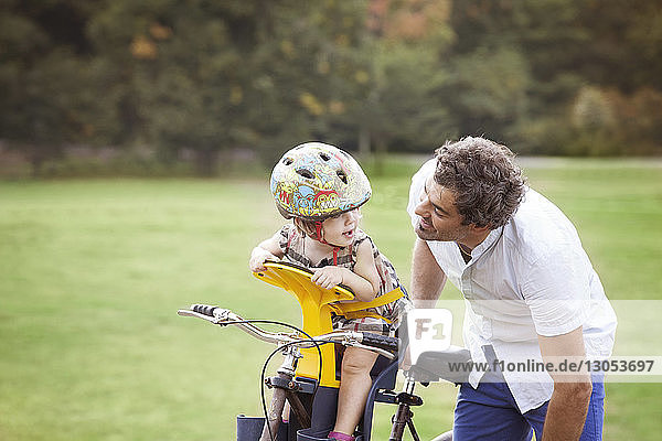 Vater sieht Tochter auf Fahrradkindersitz im Park sitzend an