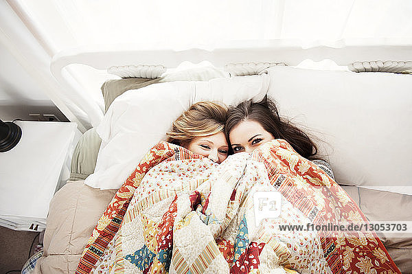 Draufsicht auf Freundinnen  die zu Hause im Bett liegend durch die Decke peppen