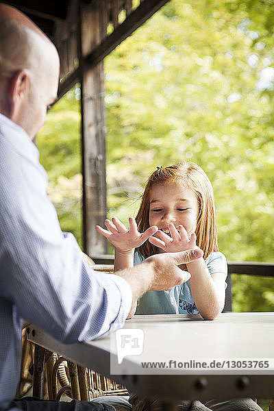 Fröhliches Mädchen spielt mit dem Vater  während sie im Pavillon am Tisch sitzt