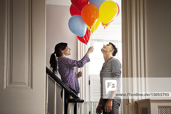 Glückliche Frau hält Heliumballons  während sie zu Hause beim Mann steht