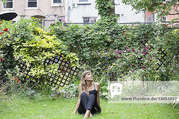 Nachdenkliche Frau sitzt auf einem Grasfeld im Hinterhof
