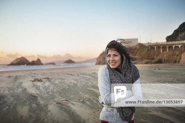Junge Frau steht am Strand mit verschränkten Armen gegen den Himmel