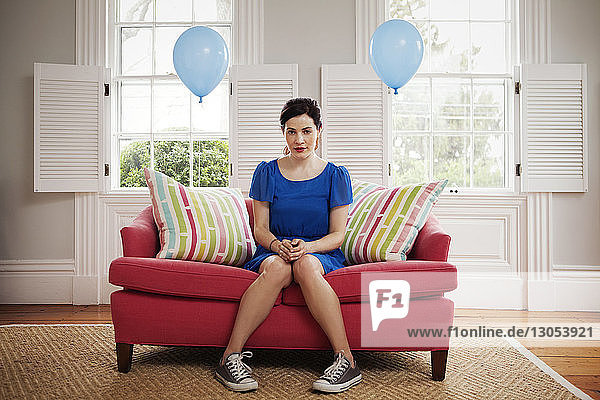 Porträt einer Frau  die zu Hause auf einem Sofa sitzt und an Heliumballons hängt