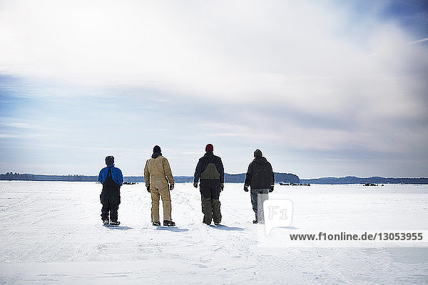 Rückansicht von männlichen Freunden  die auf einem zugefrorenen See vor bewölktem Himmel stehen