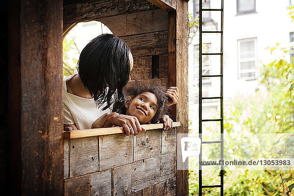 Mädchen schaut Mutter an  während sie sich auf die Fensterbank eines Baumhauses lehnt
