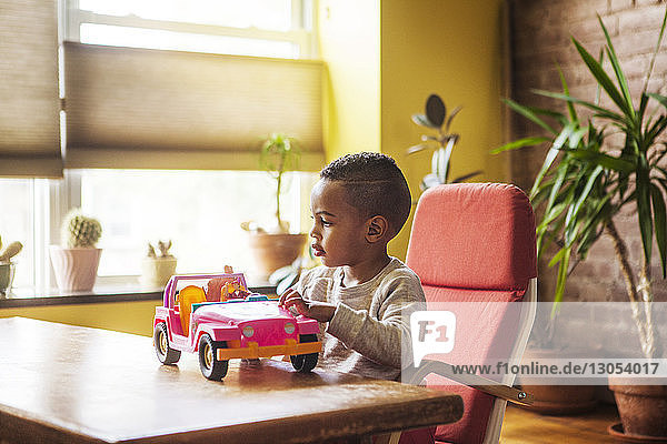 Junge spielt mit Spielzeugauto  während er zu Hause auf einem Stuhl am Tisch sitzt