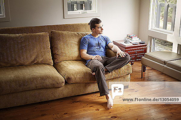 Thoughtful man looking away while relaxing on sofa