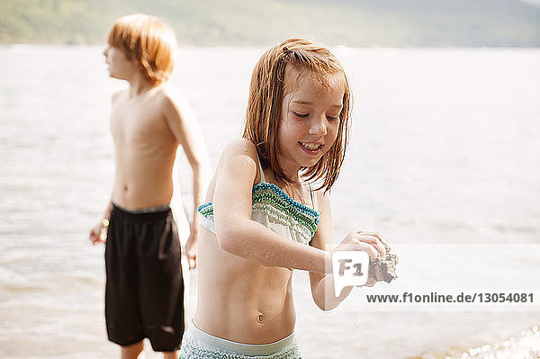 Mädchen spielt mit Sand gegen im See stehenden Bruder