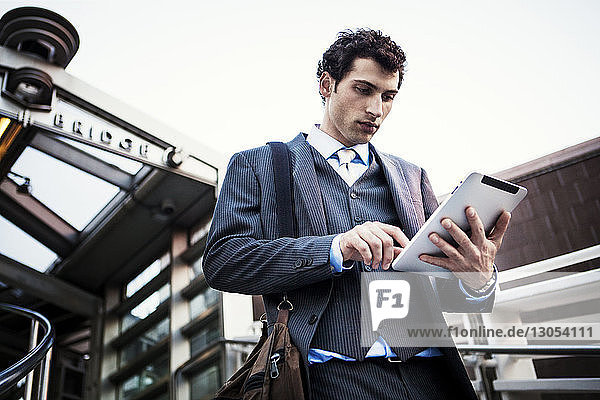 Low angle view of businessman using digital tablet against sky
