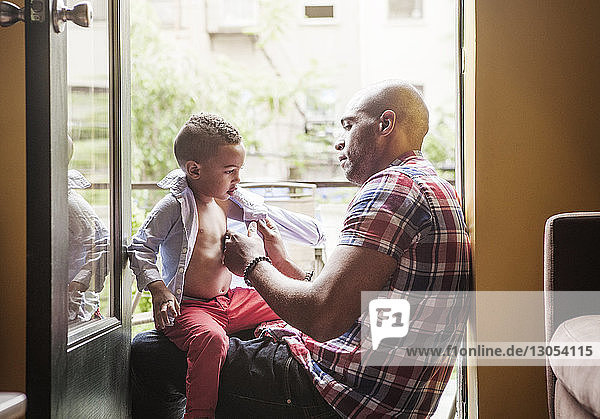 Father dressing son while sitting at entrance