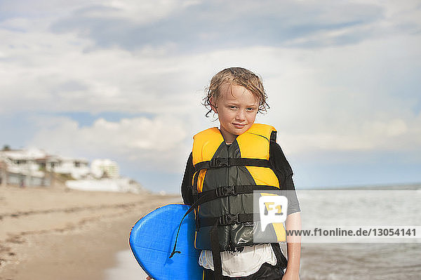 Porträt eines Jungen mit Surfbrett am Strand