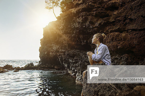 Nachdenkliche Frau sitzt auf einem Felsen am Strand