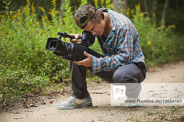 Man using video camera while crouching on dirt road
