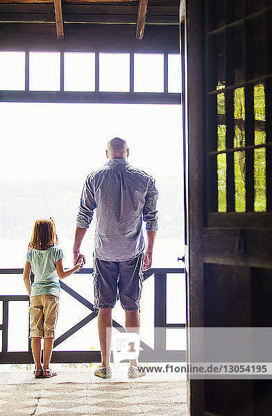 Rückansicht eines Vaters  der die Hand seiner Tochter hält  während er am Balkon steht  durch die Tür gesehen