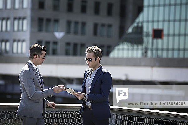 Geschäftsleute  die einen Tablet-Computer benutzen  während sie an einem Geländer vor Stadtgebäuden stehen
