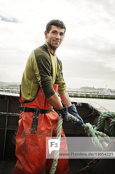 Portrait of smiling fisherman pulling rope on fishing boat against sky