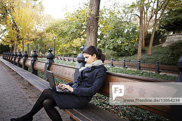 Woman using laptop while sitting on bench in Central Park