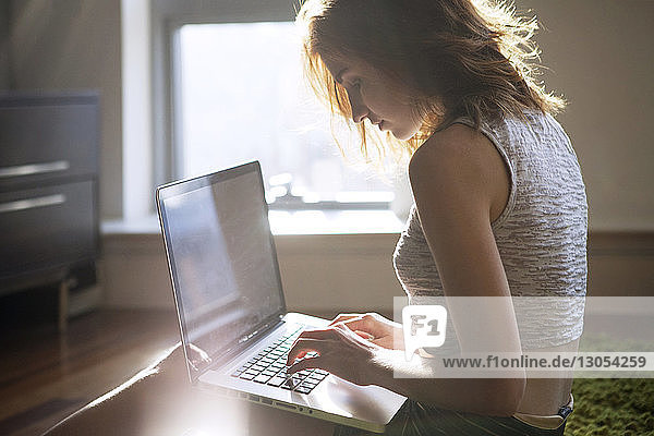 Seitenansicht einer Frau,  die zu Hause am Laptop sitzt