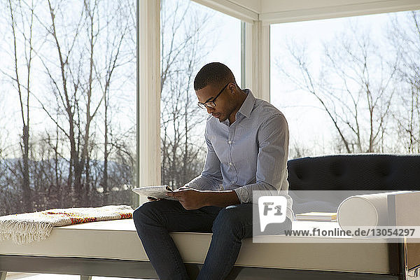 Mann liest Zeitung  während er zu Hause auf dem Sofa sitzt