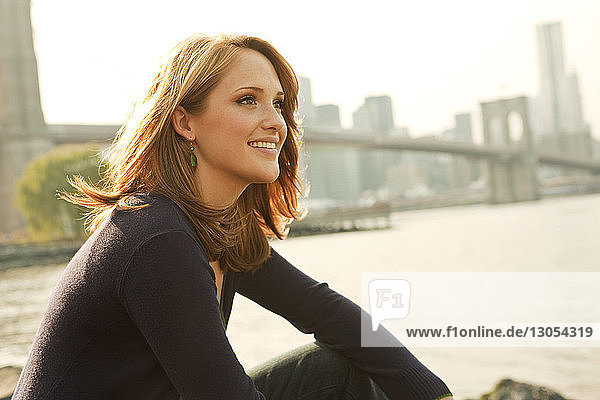 Happy thoughtful woman sitting against East River