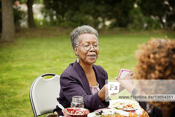 Cropped image of woman showing mobile phone to mother at table in backyard