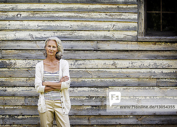 Porträt einer Frau mit verschränkten Armen vor einem Häuschen stehend