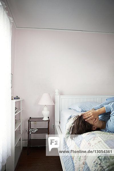 Frau bedeckt Gesicht mit Händen  während sie auf dem Bett liegt