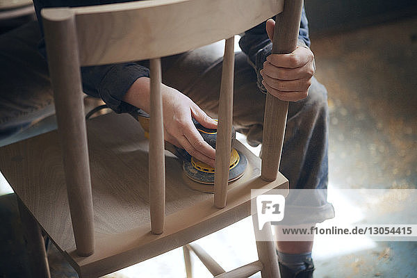 Mittelteil einer Tischlerin beim Schleifen eines Holzstuhls im Workshop