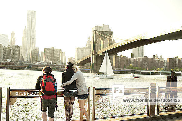 Friends standing on promenade while looking at Brooklyn bridge in city