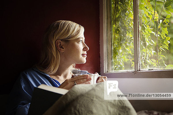 Nachdenkliche Frau schaut weg  während sie am Fenster sitzt