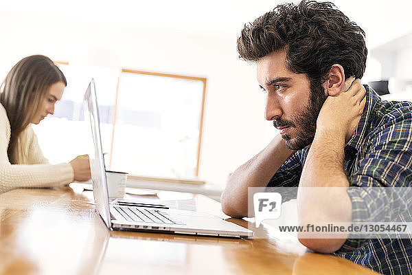 Man working on laptop while woman sitting in background
