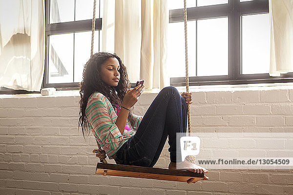 Mädchen benutzt Mobiltelefon  während sie zu Hause auf der Schaukel sitzt