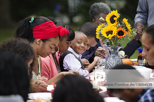 Porträt eines lächelnden Jungen  der mit Familie und Freunden bei Tisch sitzt und dabei isst