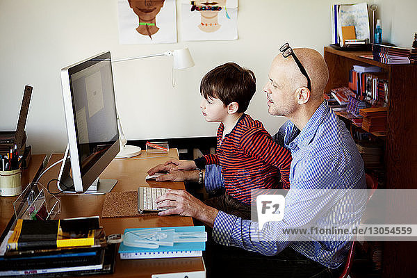 Vater und Sohn benutzen Desktop-Computer  während sie am Tisch sitzen