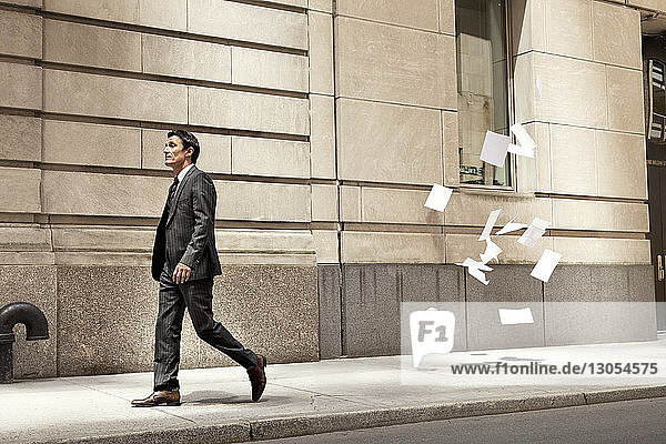 Zuversichtlicher Geschäftsmann geht  während auf der Straße in der Stadt Papiere fliegen