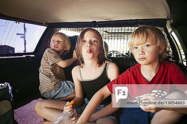 Geschwister essen  während sie im Kofferraum eines Autos sitzen
