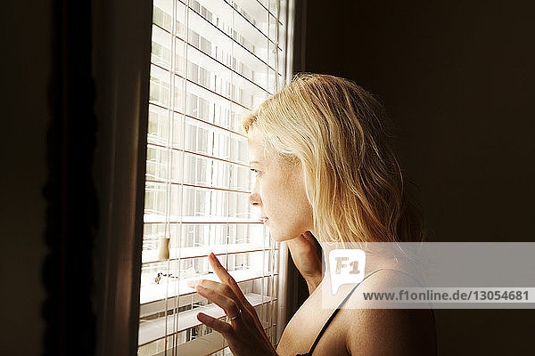 Seitenansicht einer Frau  die zu Hause durch einen Fensterladen schaut