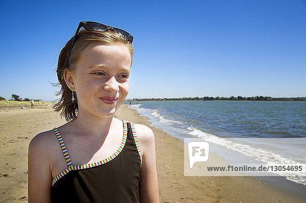 Glückliches Mädchen schaut weg  während es am Strand vor klarem Himmel steht