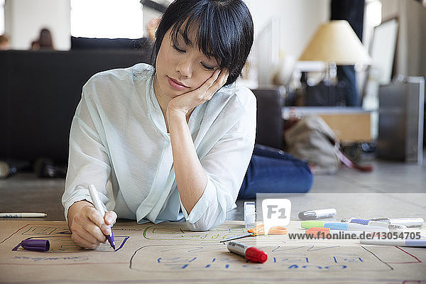 Geschäftsfrau bereitet Diagramm vor  während sie im Kreativbüro auf dem Boden liegt
