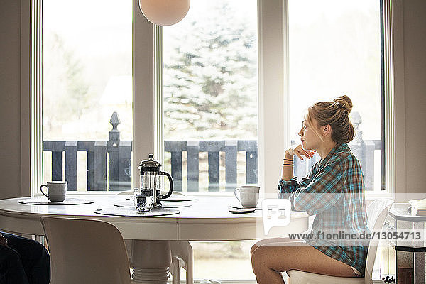 Side view of woman sitting by breakfast table in morning at home