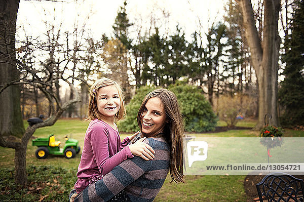 Portrait of happy mother carrying daughter in backyard