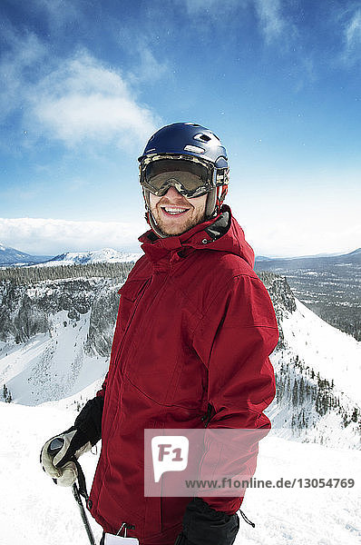 Smiling man standing on snowcapped mountain against sky