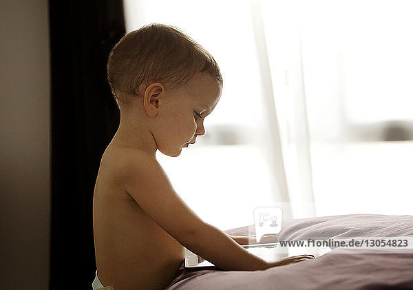 Side view of boy using tablet computer at bed in home