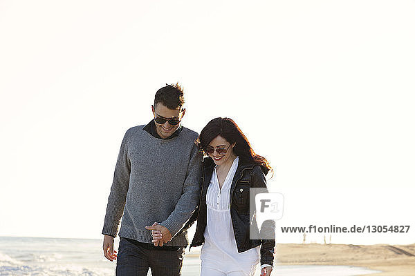 Happy couple walking at beach against clear sky