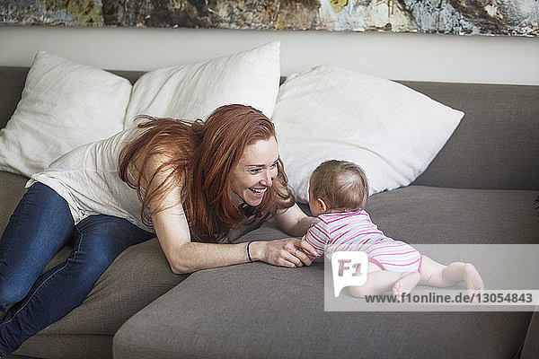Cheerful mother playing with baby girl on sofa at home